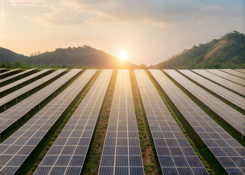 A solar panel array with green mountains and a bright sunrise in the background