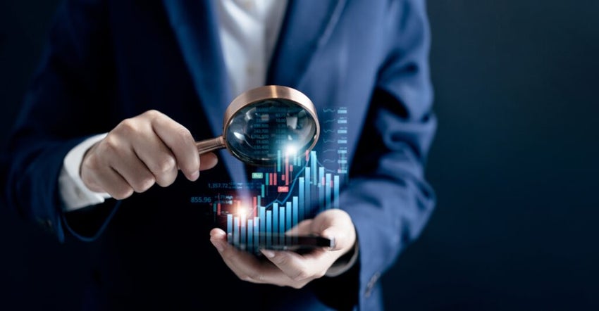 Man in suit with magnifying glass looking at uptrend graph