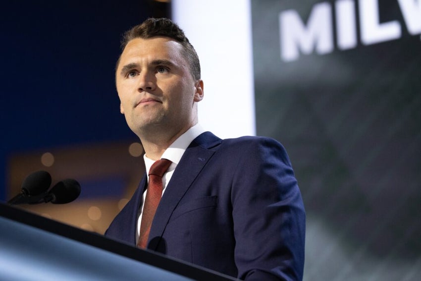 Charlie Kirk in a suit speaking at a podium