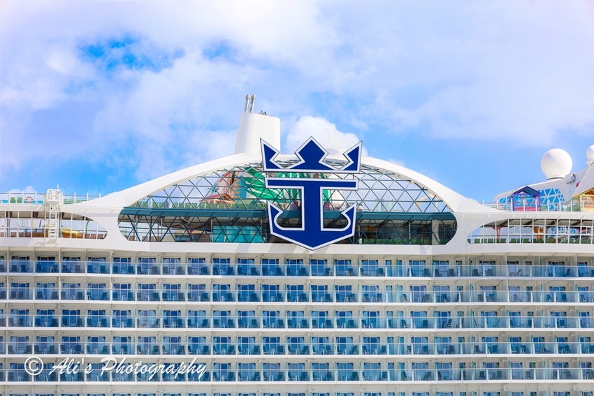 A low-angle, close-up shot of the front of a large Royal Caribbean cruise ship against a blue sky with white clouds.