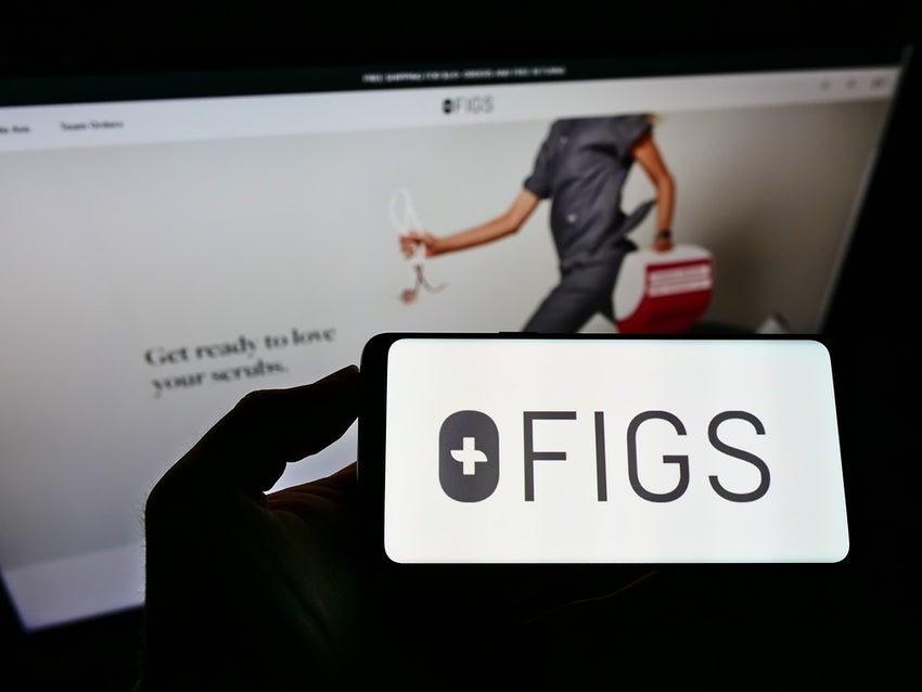 Healthcare worker in scrubs in background of phone with Figs logo