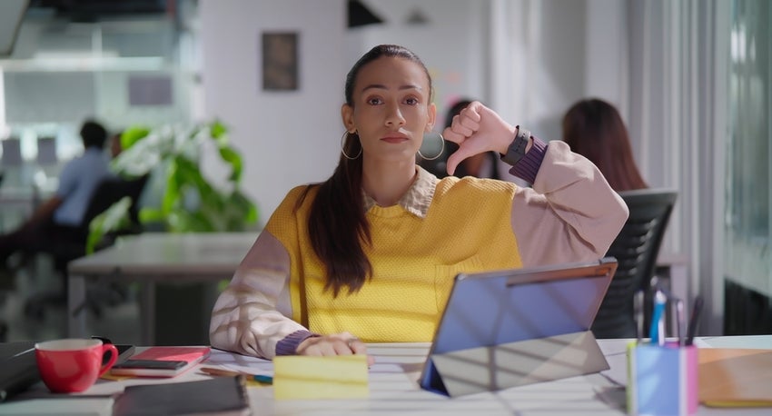A young woman at a desk making a thumbs-down motion