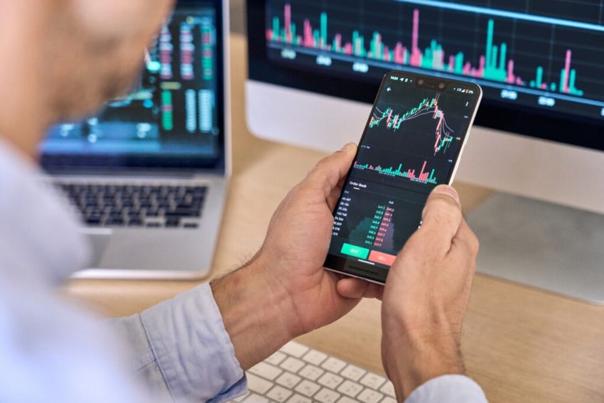 Person analyzing stock charts on smartphone and computer screens