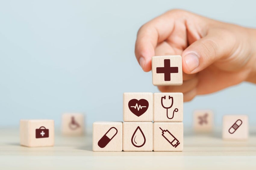 Hand placing a wooden block featuring health and medical icons, symbolizing insurance, healthcare, and medicine.