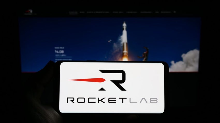 Person holding smartphone with logo of aerospace company Rocket Lab USA Inc. on screen in front of website.