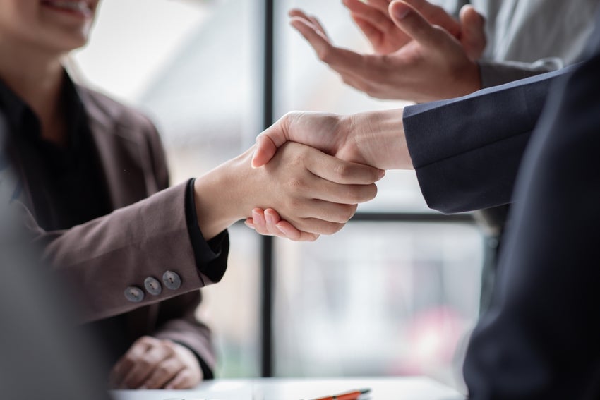 Two people shaking hands others clapping nearby.