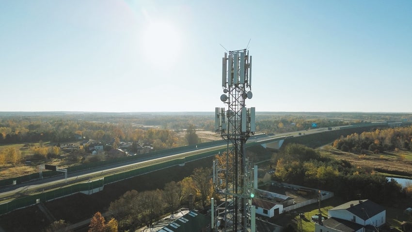 Cell tower near highway in rural landscape sunny day.