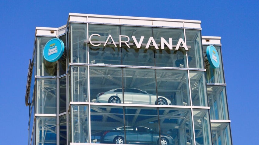Glass Carvana tower with parked cars, branded signage, and clear blue sky.