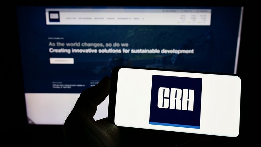 Person holding smartphone with logo of building materials company CRH plc on screen in front of website.