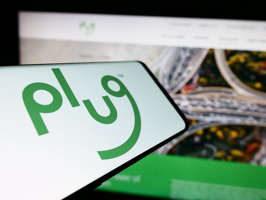 A smartphone displaying the green plug logo of Plug Power, placed on a surface next to a laptop showing a similar green-themed webpage.