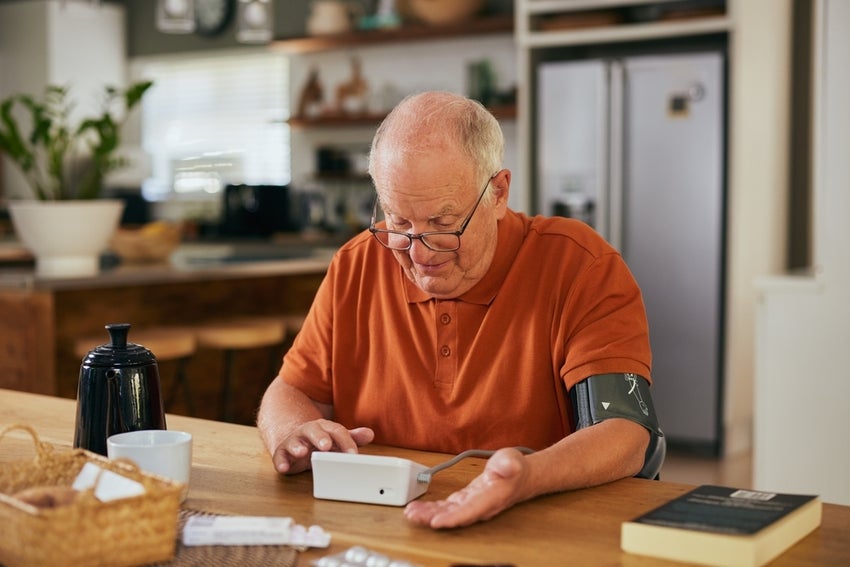 Elderly man checking heart and blood pressure at home with a digital device.