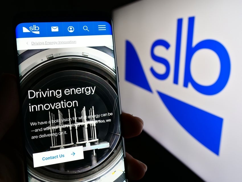 Person holding cellphone with webpage of oilfield company SLB Limited on screen in front of logo. Focus on center of phone display.