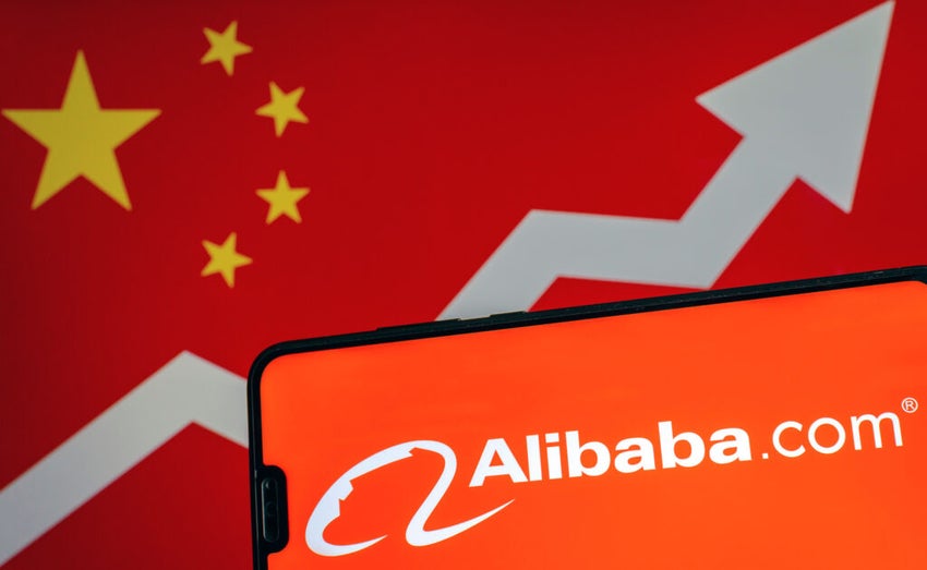 Alibaba logo on smartphone and blurred screen with flag of China with arrow at the background.