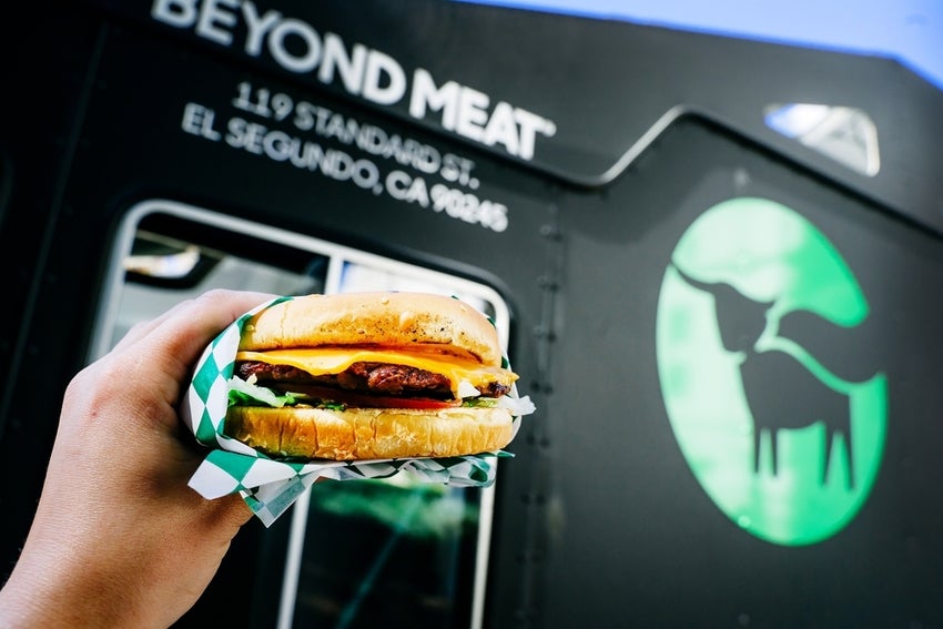 Hand holding a hamburger with Beyond Meat logo in the background.