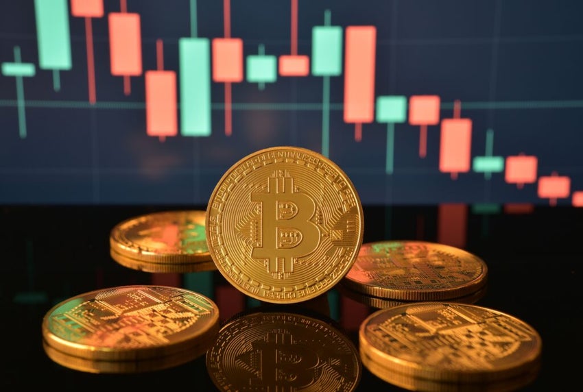 London, UK - January 26, 2024: Photograph of golden Bitcoin, pile of coins on black reflective surface and price fall or decline candlestick chart on background. High volatility investment.