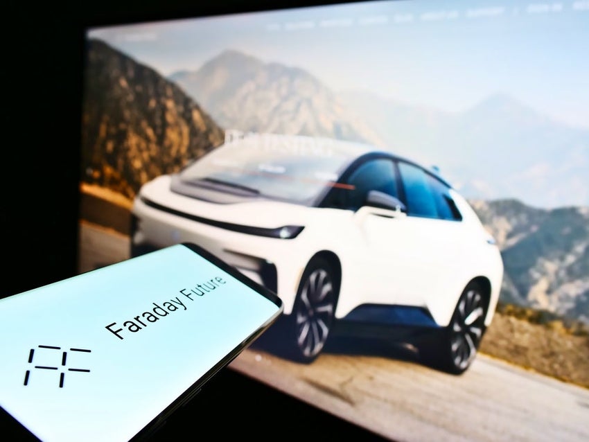 Cellphone with business logo of American electric vehicle company Faraday Future Inc. in front of web page.