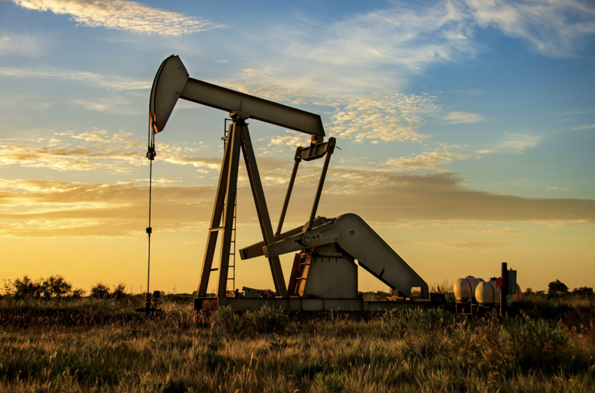 Oil pumpjack in grassy field at sunset.
