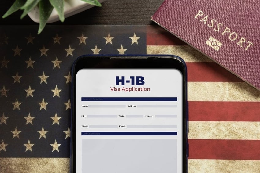 An H-1B visa application form displayed on a tablet with the U.S. flag in the background