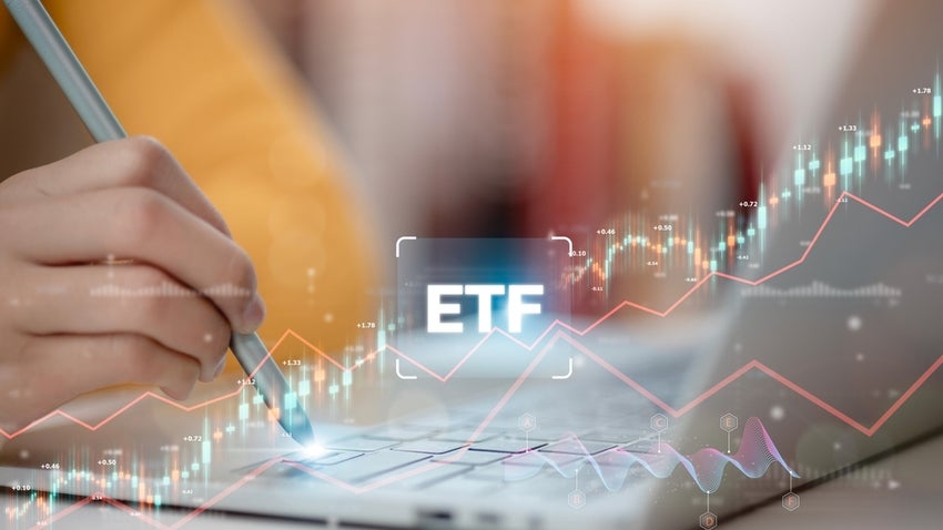 Hand holding a pen over a laptop with 'ETF' superimposed over it, indicating stocks rising