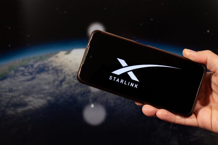 BOGOTA, COLOMBIA - JULY 14 OF 2025 A male hand holding a smartphone with his right hand with Starlink logo and a blurred planet earth in space at background