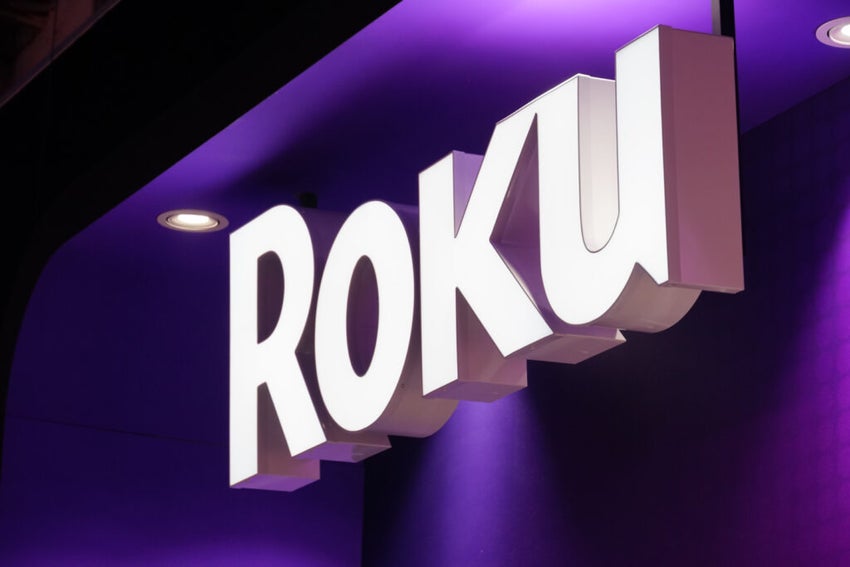 Hand holding Roku remote in front of streaming service apps on TV