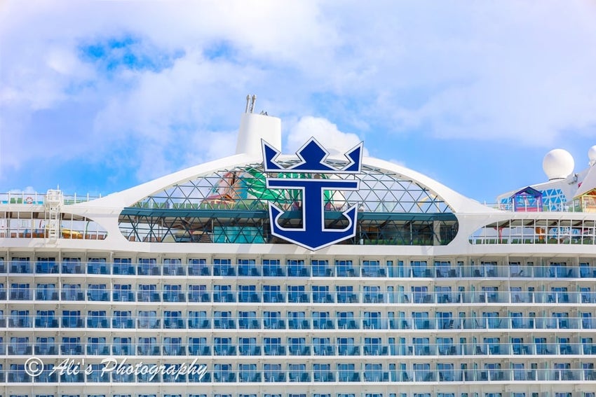 A low-angle, close-up shot of the front of a large Royal Caribbean cruise ship against a blue sky with white clouds.
